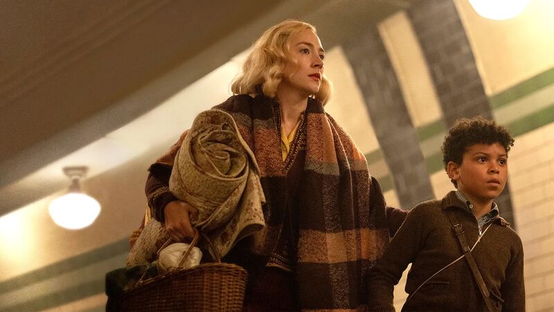 A blonde woman in 1940s clothes walks through London Underground with a little boy.