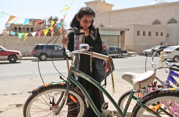 A young girl stands outside on a street in Saudi Arabia, looking at a green bicycle 