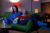 Two women sit on a green sofa together watching television.