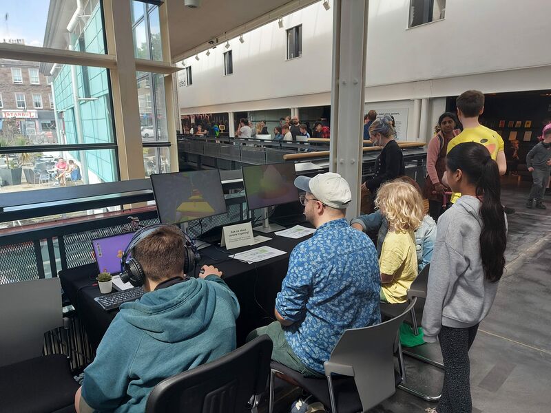 A group of people of all ages watch children playing games at Drop in and Play 2024.