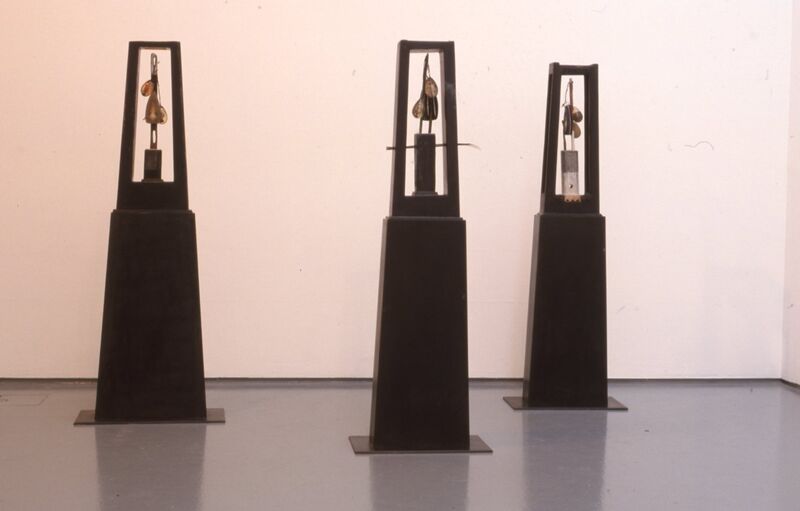 Black plinth-like statues with small figures standing on them.