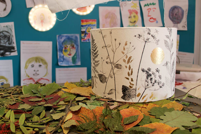 Lampshade on a table beside a selection of leaves. The lampshade is printed with a plant design and gold foil details