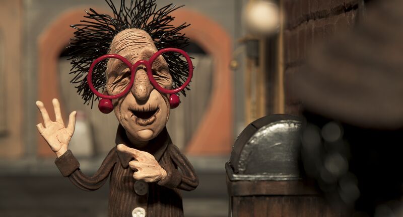 A claymation still of an older woman wearing large red glasses with spiky dark hair.