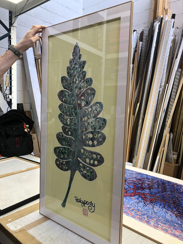 Person holding a large framed wood cutprint of a leaf by Tom Scott