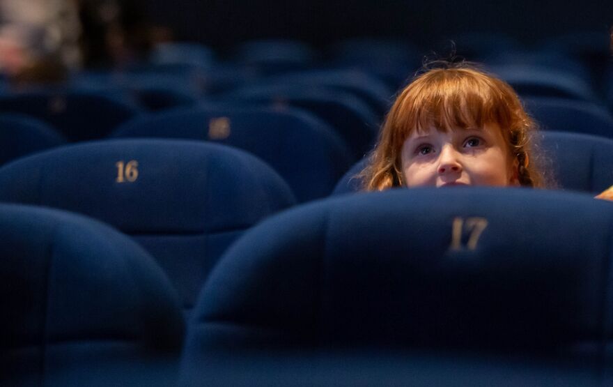 Girl with red hair smiles as she watches a film in the cinema