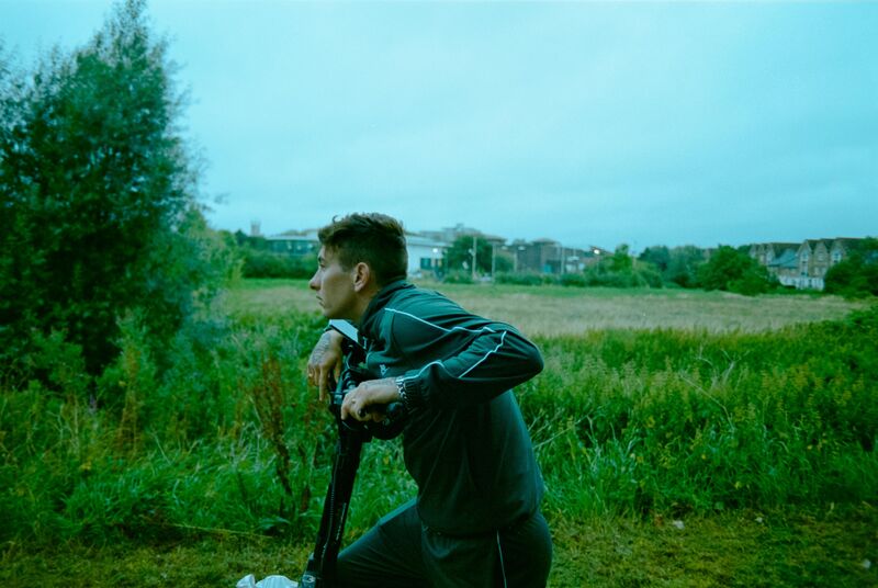 A man leans on an electric scooter in a field.