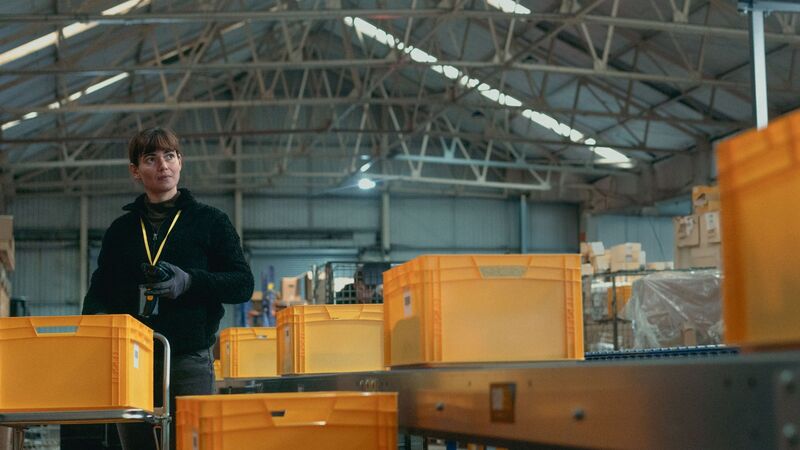 A woman on a factory floor, packing yellow crates