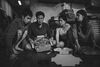 A black-and-white film still shows four people sitting on the floor, packing pizza boxes.