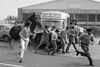 Men run, while a police officer on a horse beats them.