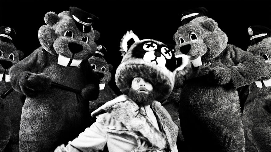 A bearded man is surrounded by people in huge beaver costumes