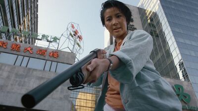 A woman points a gun with a silencer on it at the ground.