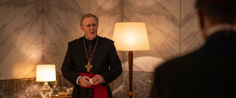 A man dressed in priest's clothes, with a cross pendant.