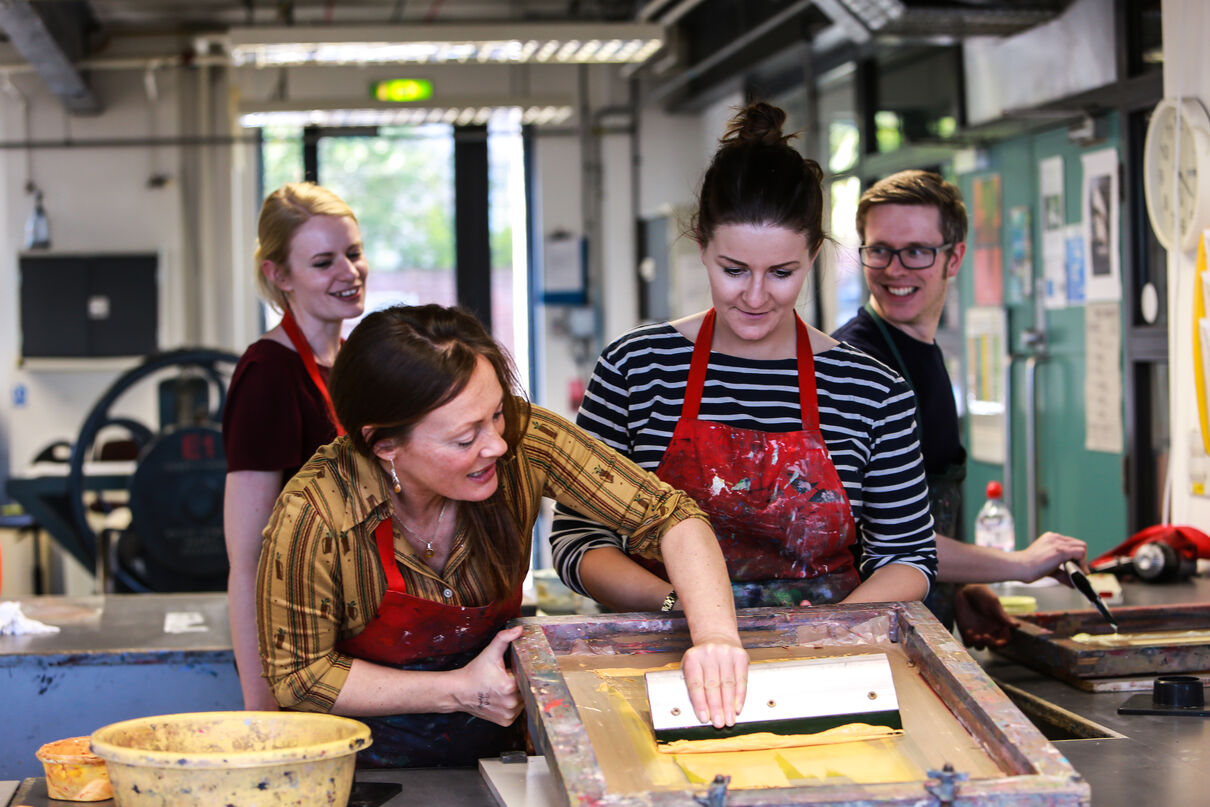 Tutor helping a person to pull a screen print while other class members watch