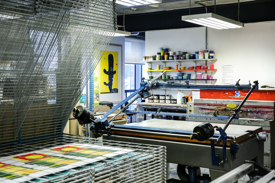 A print studio with a large screen-printing screen and drier visible colourful ink pots in the background